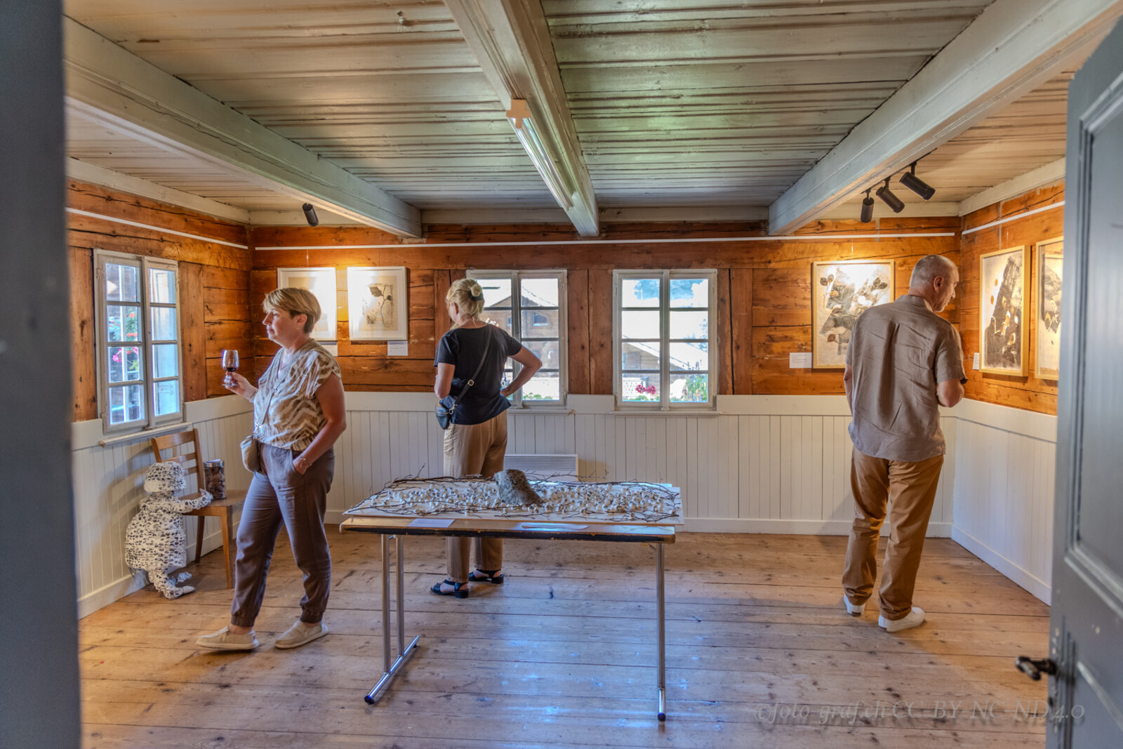Visitors in the exhibition room with framed works on the walls.