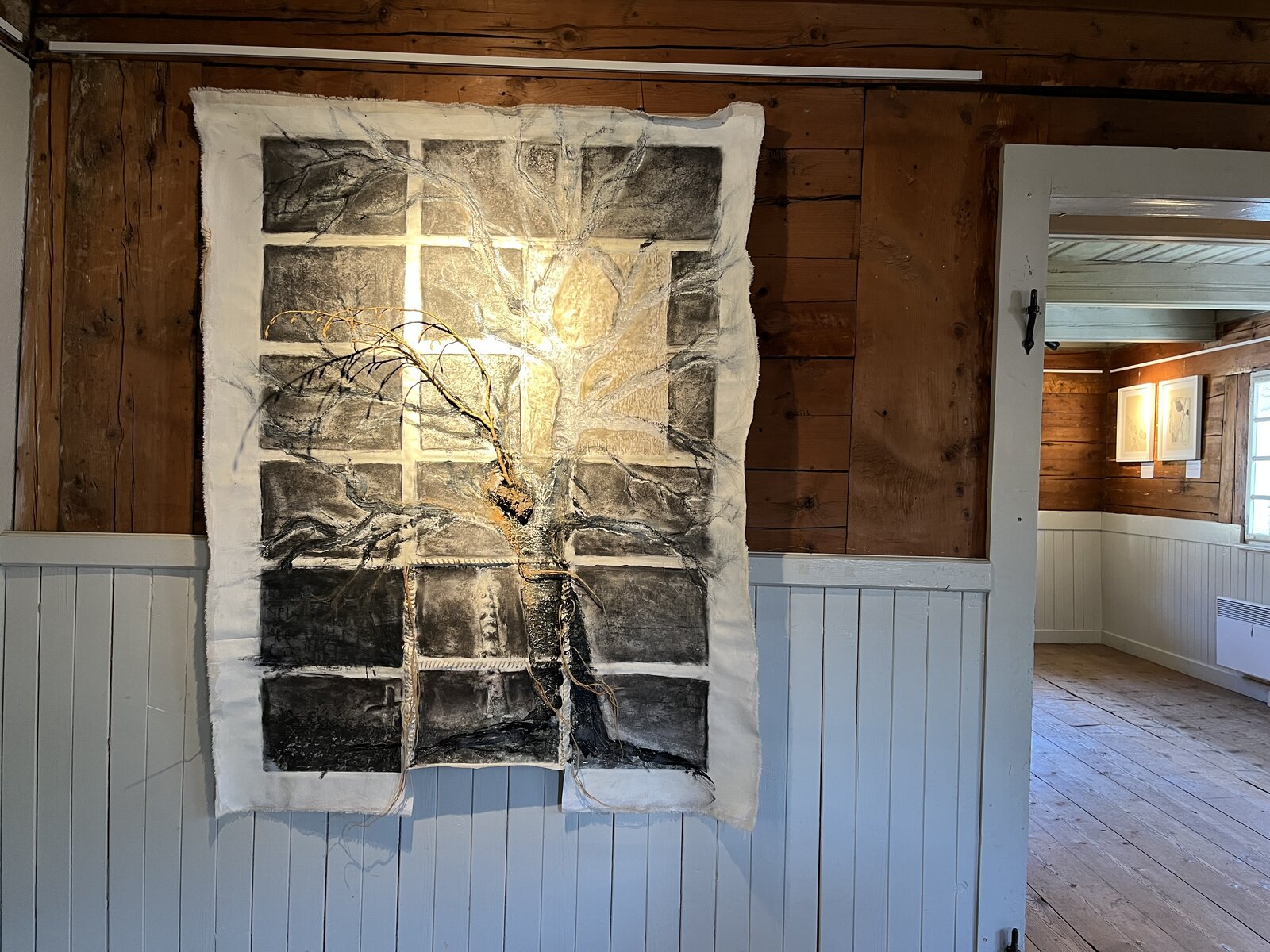 Mixed-media tapestry piece with a real branch, installed in a wood-panelled room.
